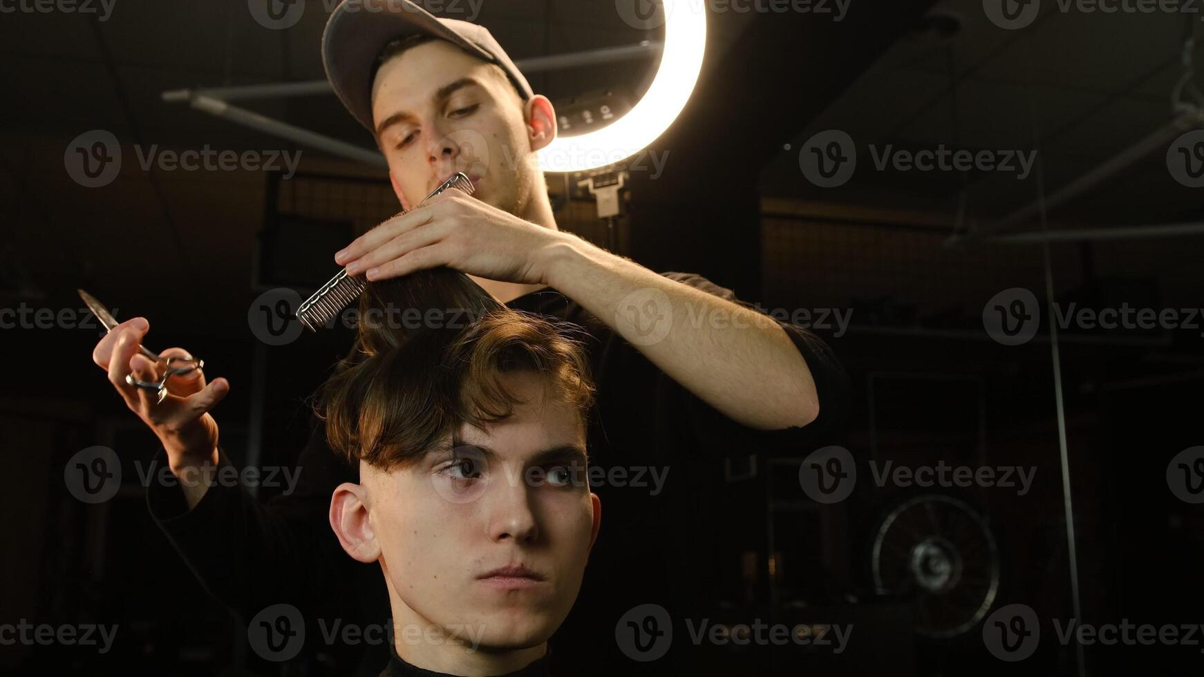 Barber master hairdresser does hairstyle and style with scissors and comb. Concept Barbershop. front view in dark key lightning with warm light photo