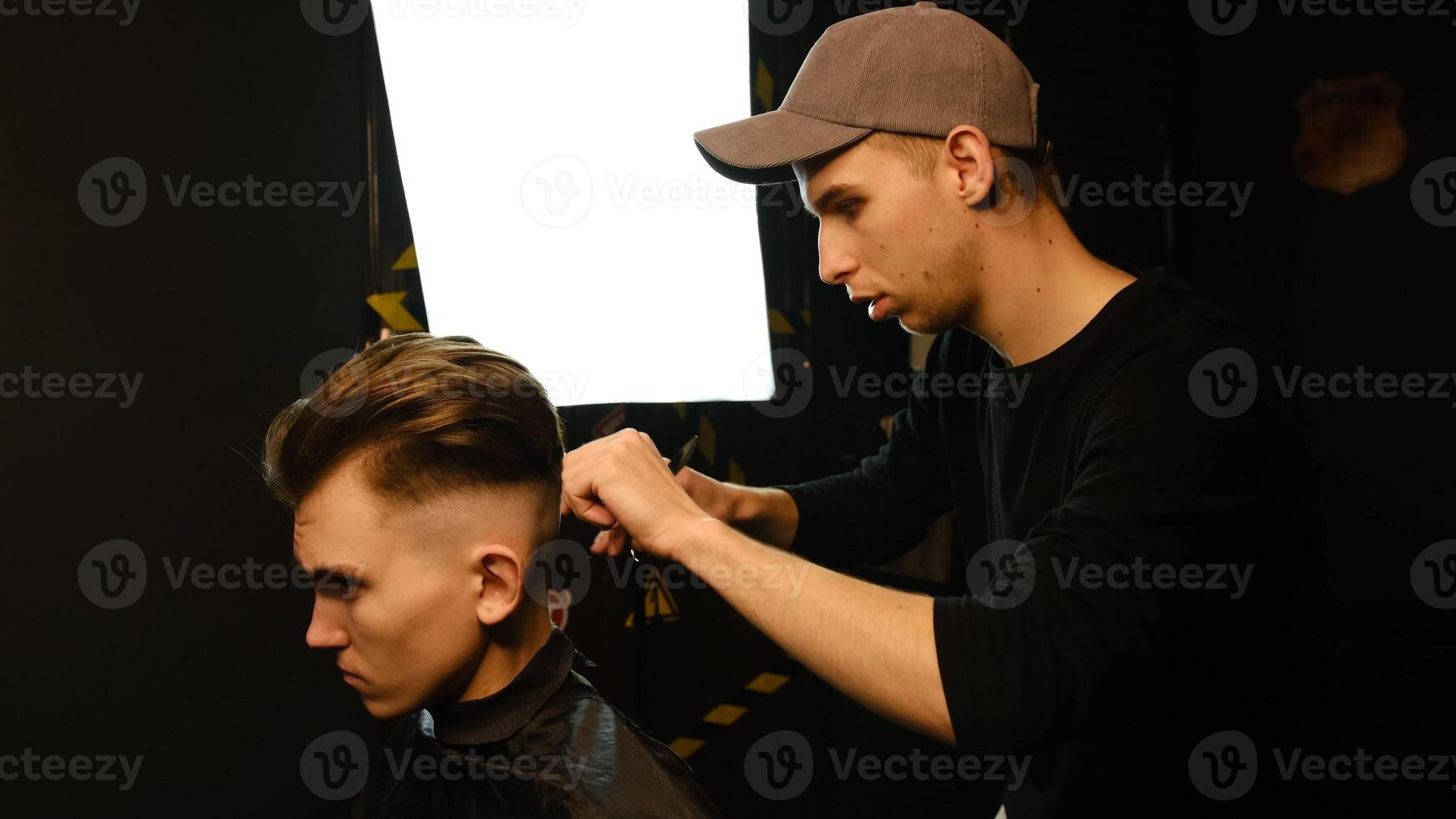 Barber master hairdresser does hairstyle and style with scissors and comb. Concept Barbershop. side view in dark key lightning with warm light photo