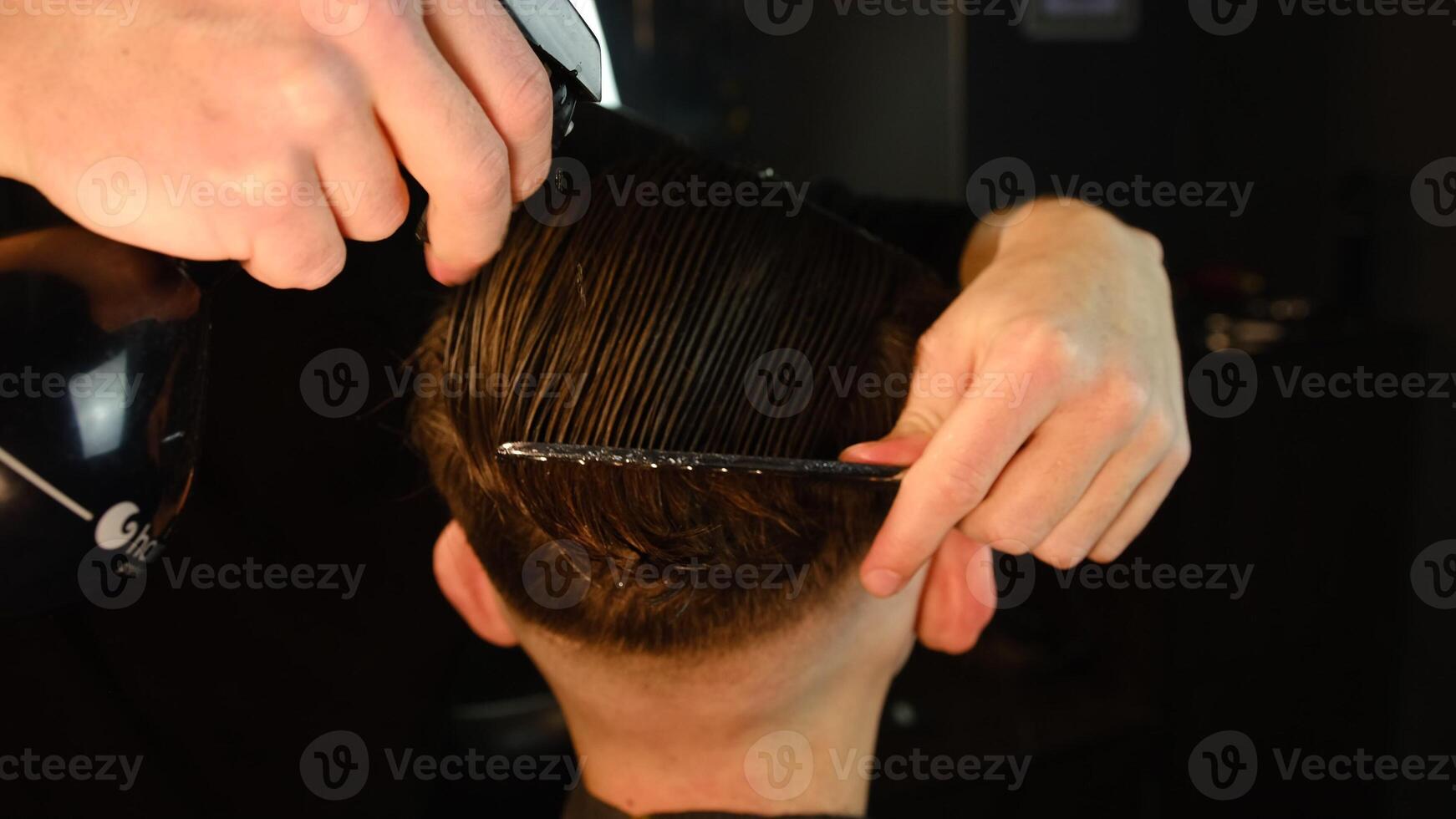 Spraying hair. barber spraying water on the hair of the client and comb it for cutting and styling. Concept Barbershop. back view in dark key lightning with warm light photo