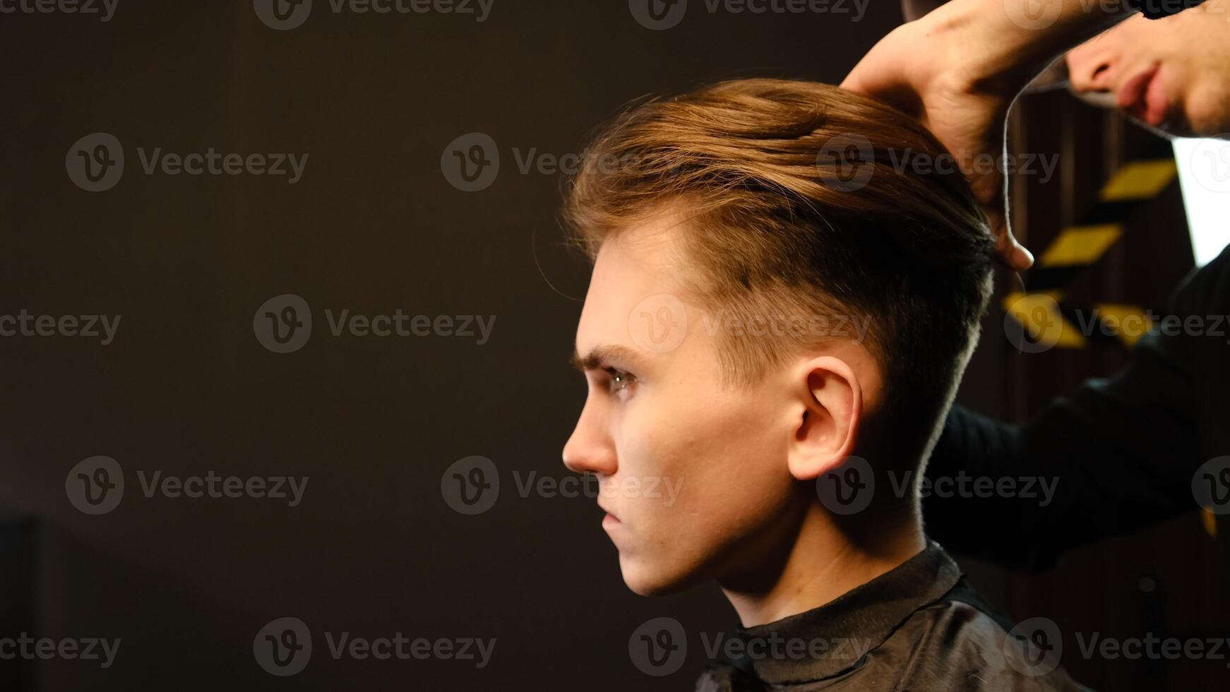 Barber shop. Man in barber's chair, hairdresser prepare his hair with comb for cutting and styling it. Concept Barbershop. side view in dark key lightning with warm light photo