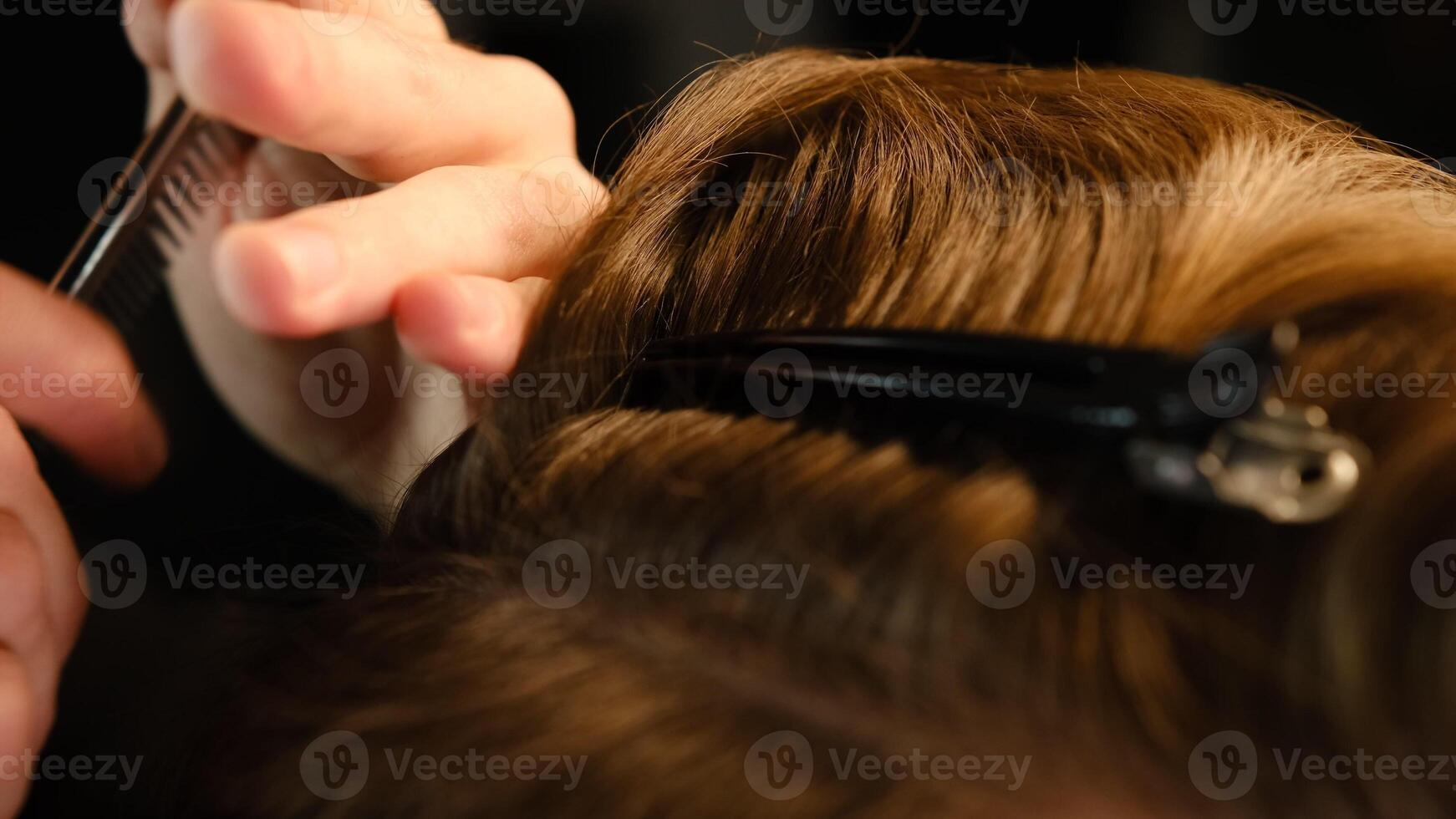 Closeup View Of barber using hair clip to fix the hair for cut and styling it. Hairdresser use pinsn hair salon. service in a modern barbershop in a dark key lightning with warm light back view photo