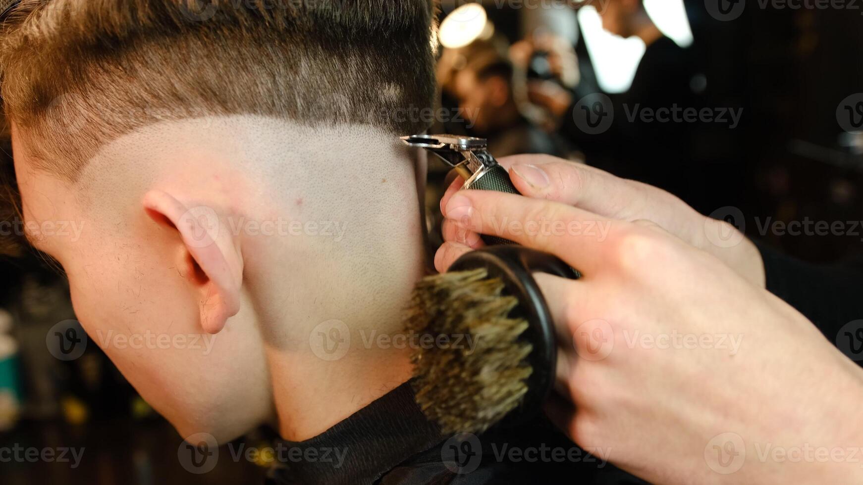 Shot of a handsome barber giving a haircut to his client using trimmer. Hairdresser service in a modern barbershop in a dark key lightning with warm light side view photo