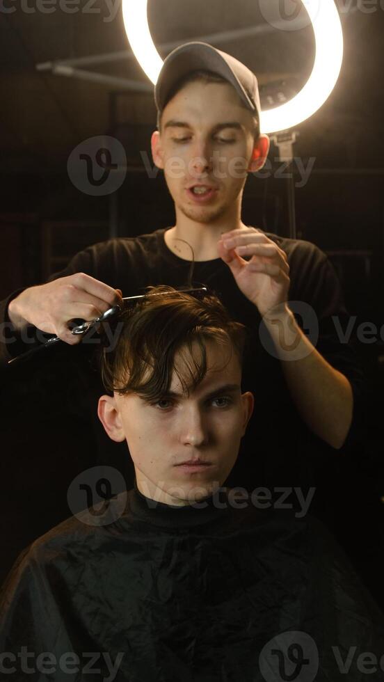 Barber master hairdresser does hairstyle and style with scissors and comb. Concept Barbershop. front view in dark key lightning with warm light photo