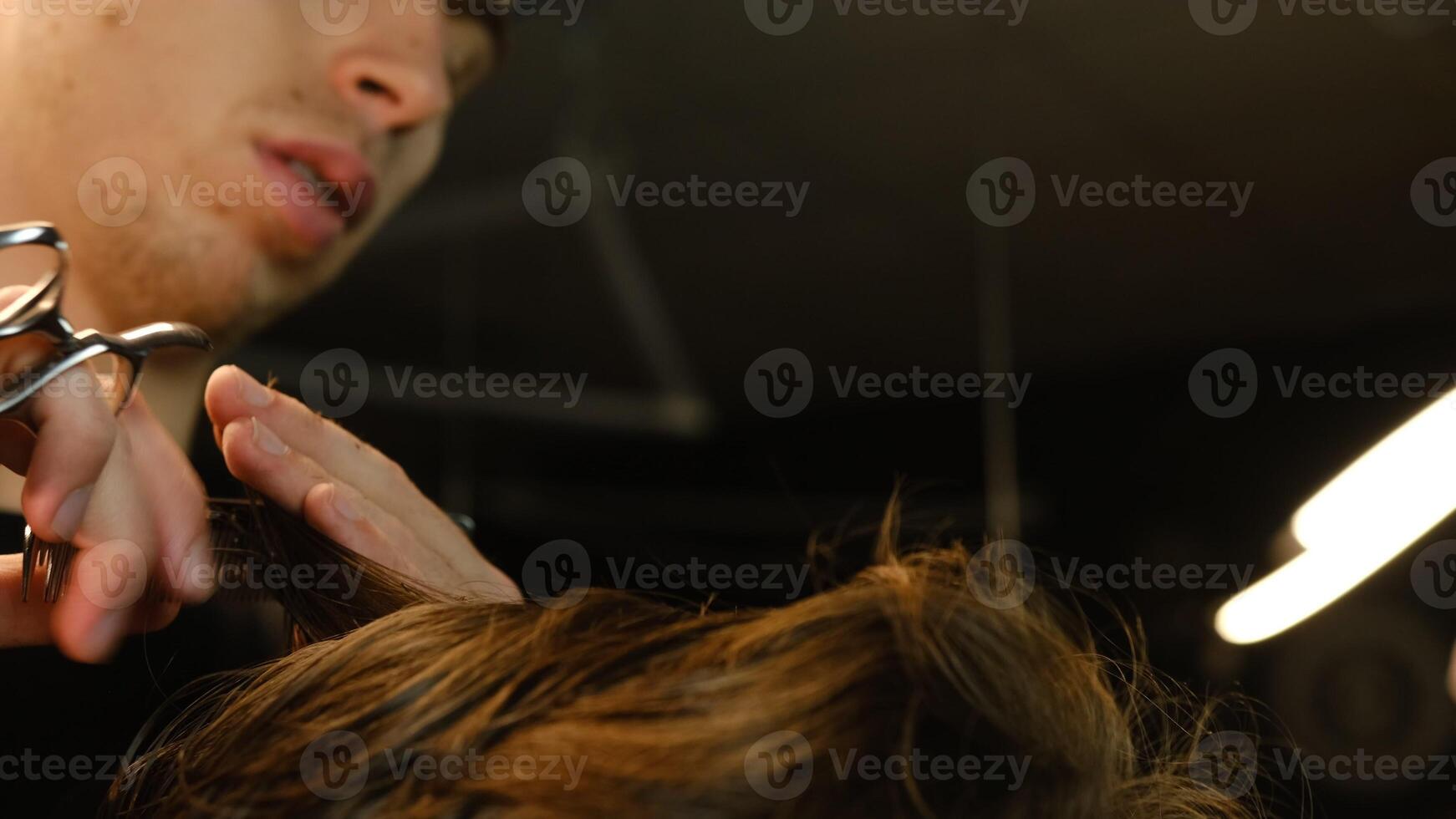 Close up Barber master hairdresser does hairstyle and style with scissors and comb. Concept Barbershop. side view in dark key lightning with warm light photo