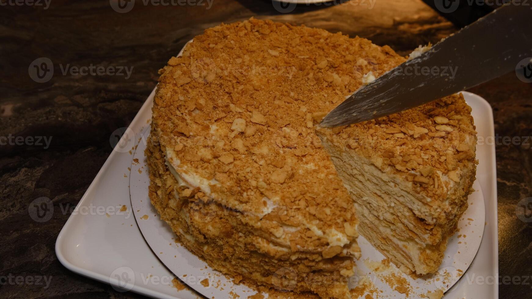 Man cuting delicious homemade puff pastry cake napoleon layered with custard cream on white plate with a piece on a cake shovel, view from above, close-up photo