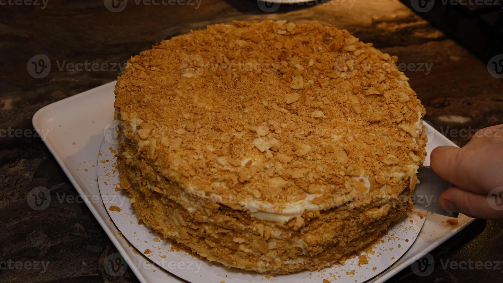 Man cuting delicious homemade puff pastry cake napoleon layered with custard cream on white plate with a piece on a cake shovel, view from above, close-up photo