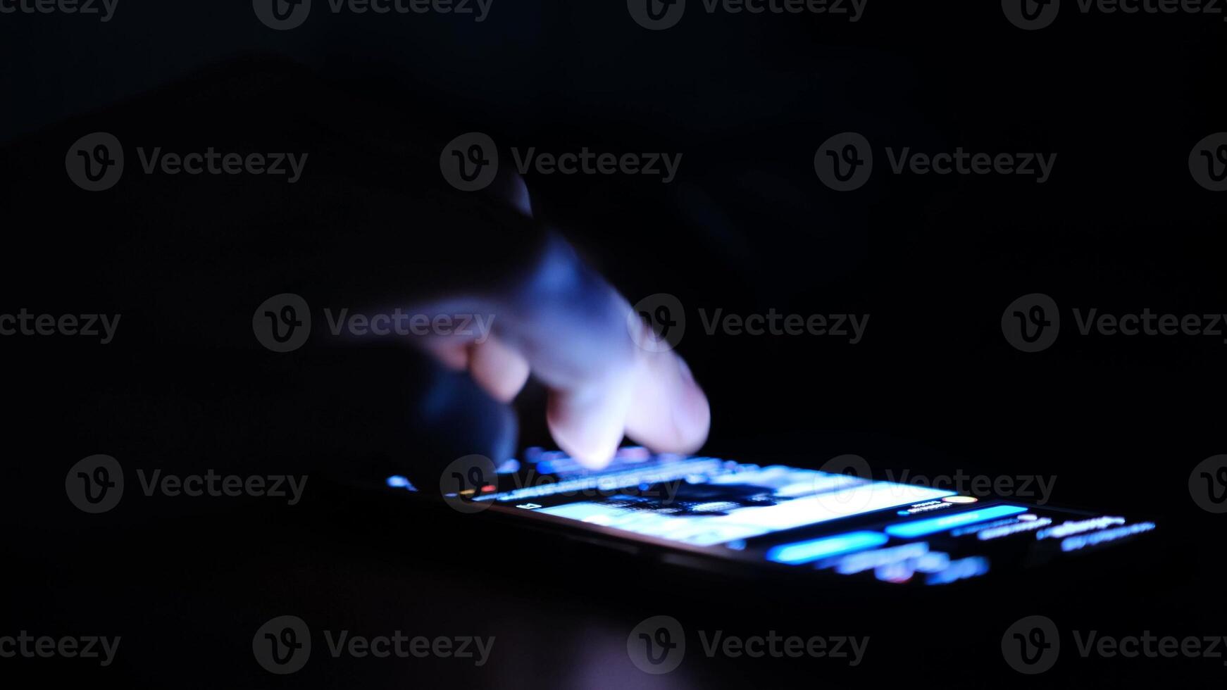 Close up of man finger using and touching on smartphone screen with reflection and black background in the darkness. Social network surfing, instagram or facebook or tiktok photo