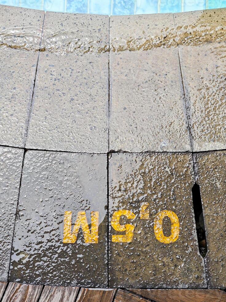 Yellow depth information 0.5 M painted on wet stone tiles at the edge of a pool with blue water. photo