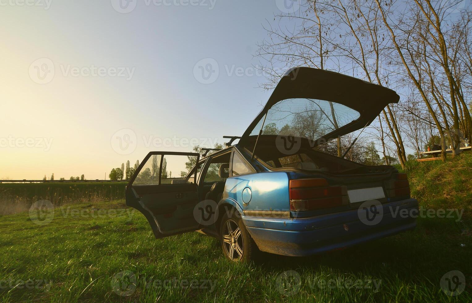 A blue car on a background of a rustic landscape with a wild cane field and a small lake. The family came to rest on the nature near the lake photo