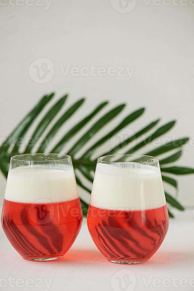 Cocktail in transparent glasses. Layers of jelly and whipped cream. Strawberry cocktail on a white background with a leaf of palm tree.Exotic. photo