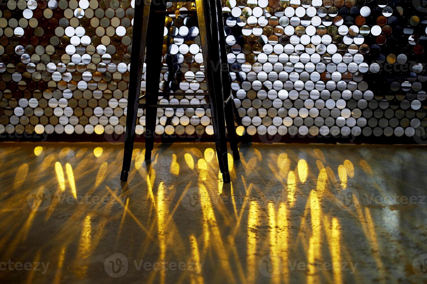 High stool on a metal base against the background of the wall with sequins. The glare is reflected on the floor. Glamorous design photo
