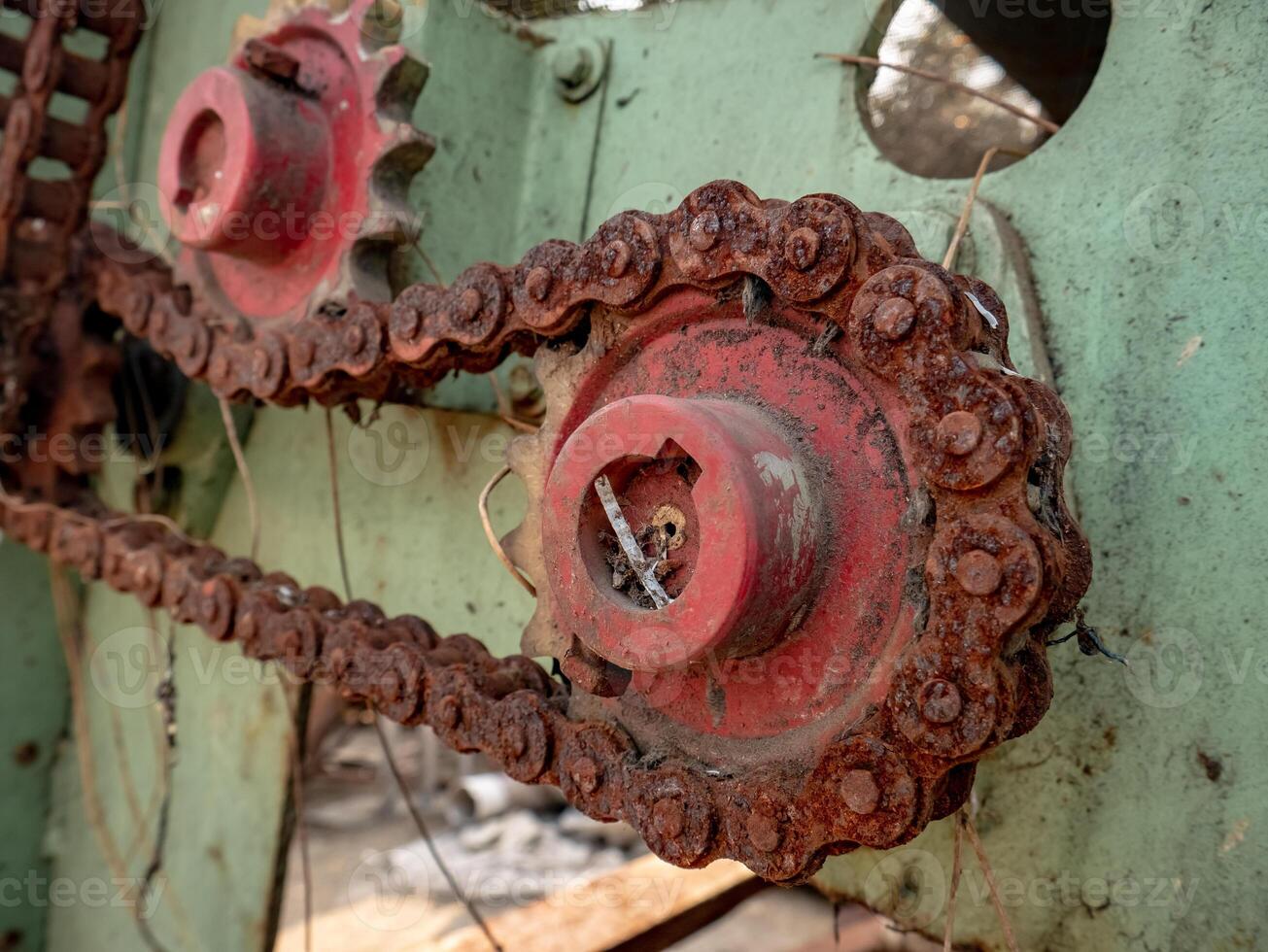 a rusty chain still attached to the red gear on an old machine with a faded green color photo