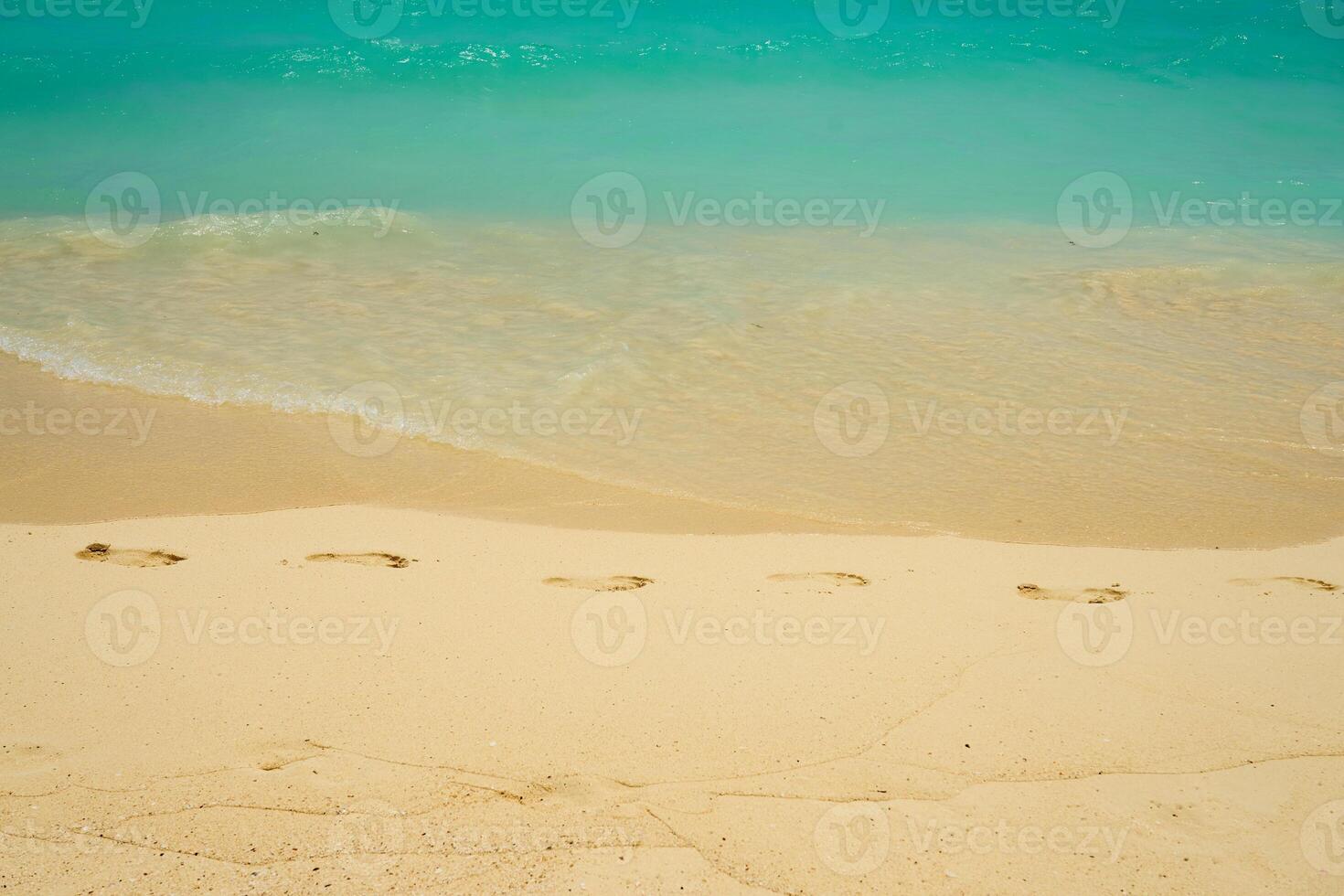 Waves and foam on a tropical sandy beach with footprints on sand photo