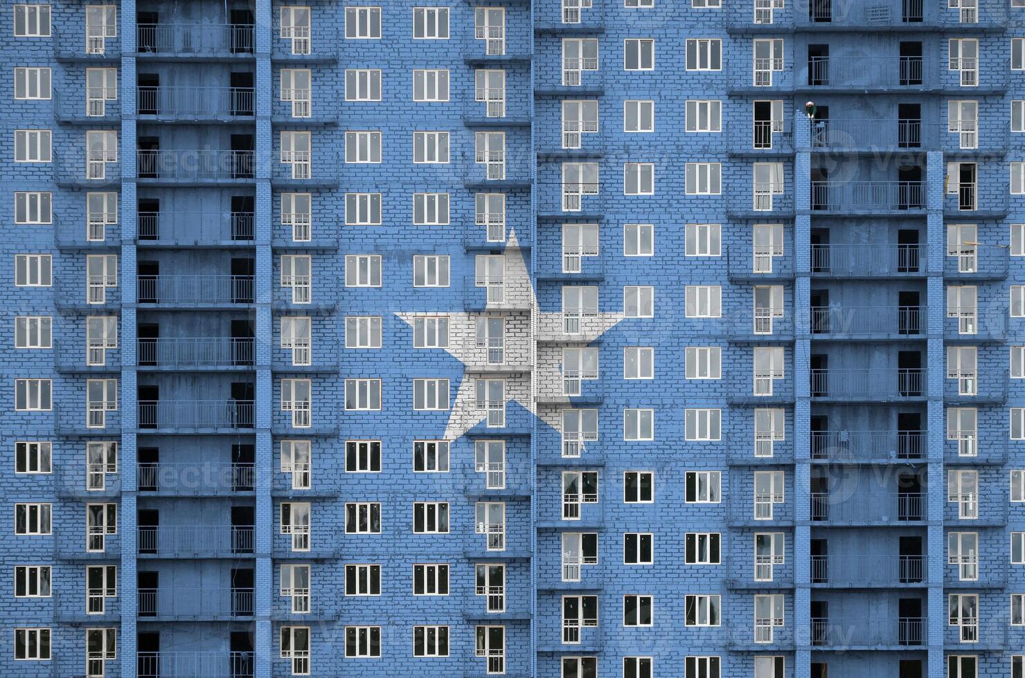 Somalia flag depicted in paint colors on multi-storey residental building under construction. Textured banner on brick wall background photo
