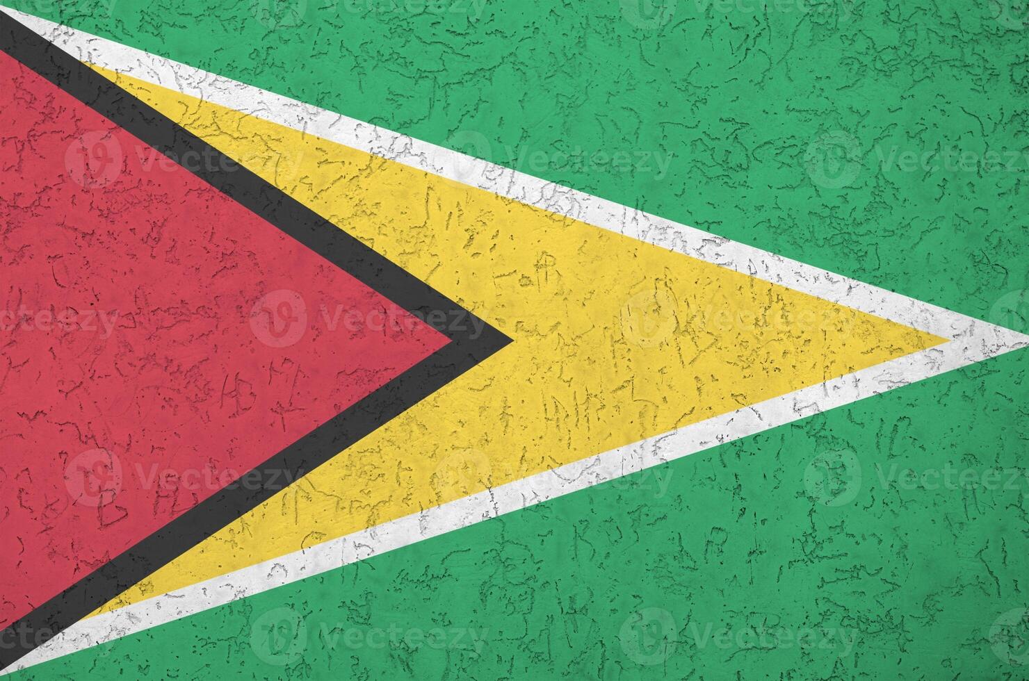 Guyana flag depicted in bright paint colors on old relief plastering wall. Textured banner on rough background photo