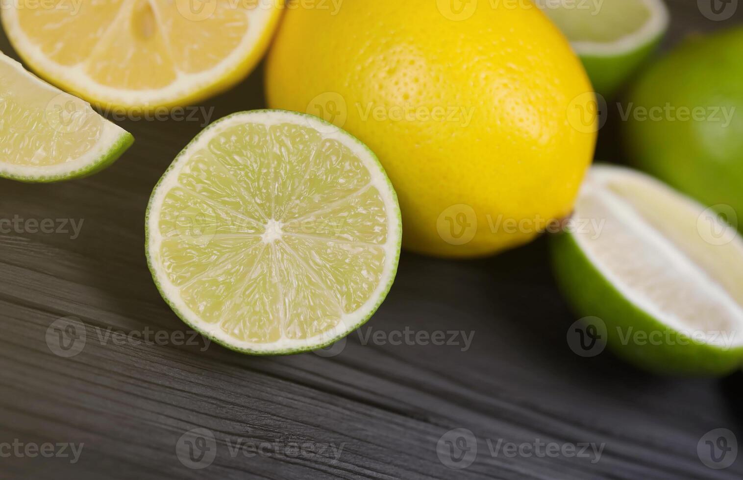 Many halves and slices of yellow lemon and green lime on black wooden table. Fresh fruits on kitchen top with copy space for text photo