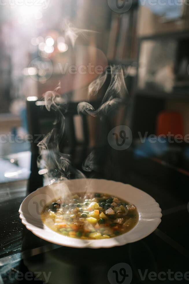 Plate of hot steaming vegetable soup on the table in the room photo