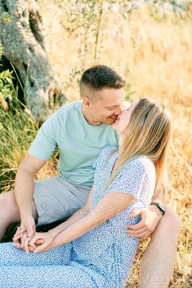Guy almost kisses girl while sitting with her on dry grass in the garden photo