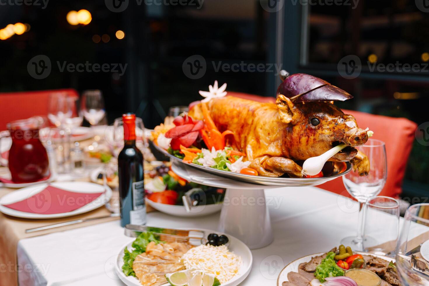 Baked pig on a dish decorated with vegetables and herbs stands on a table in a restaurant photo