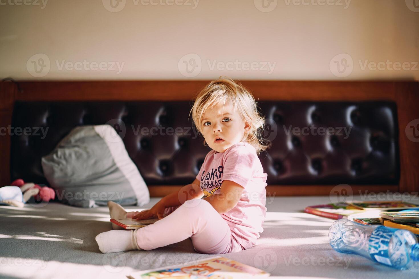 Little girl with colorful books sits on the bed photo