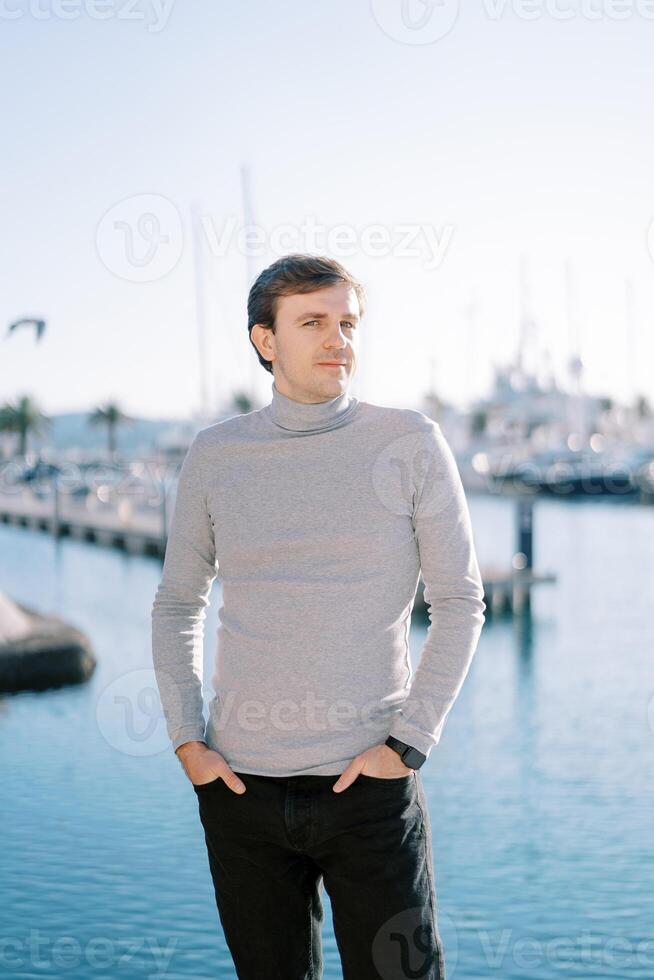 Young smiling man with his hands in his trouser pockets stands sideways on the embankment photo
