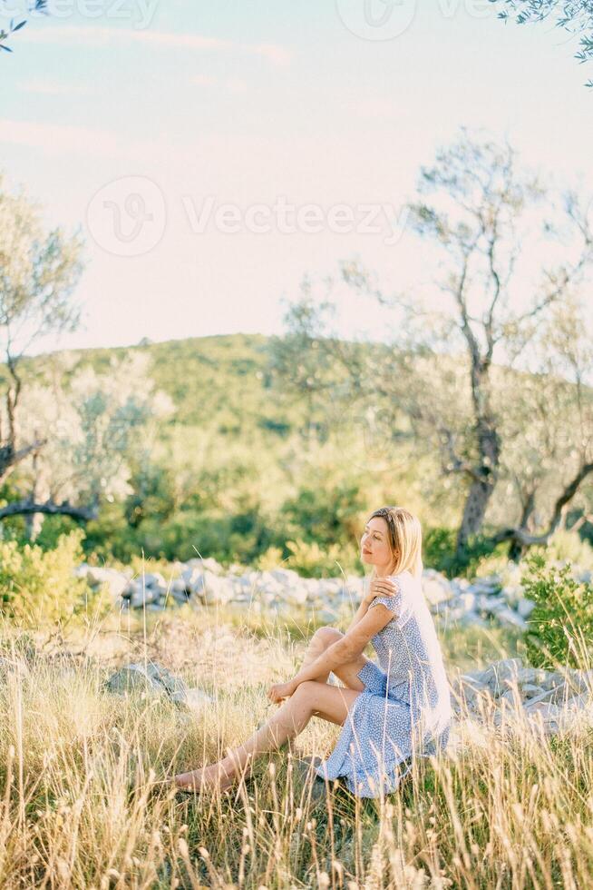 Young woman sits hugging herself by the shoulders in a green park and looks away photo