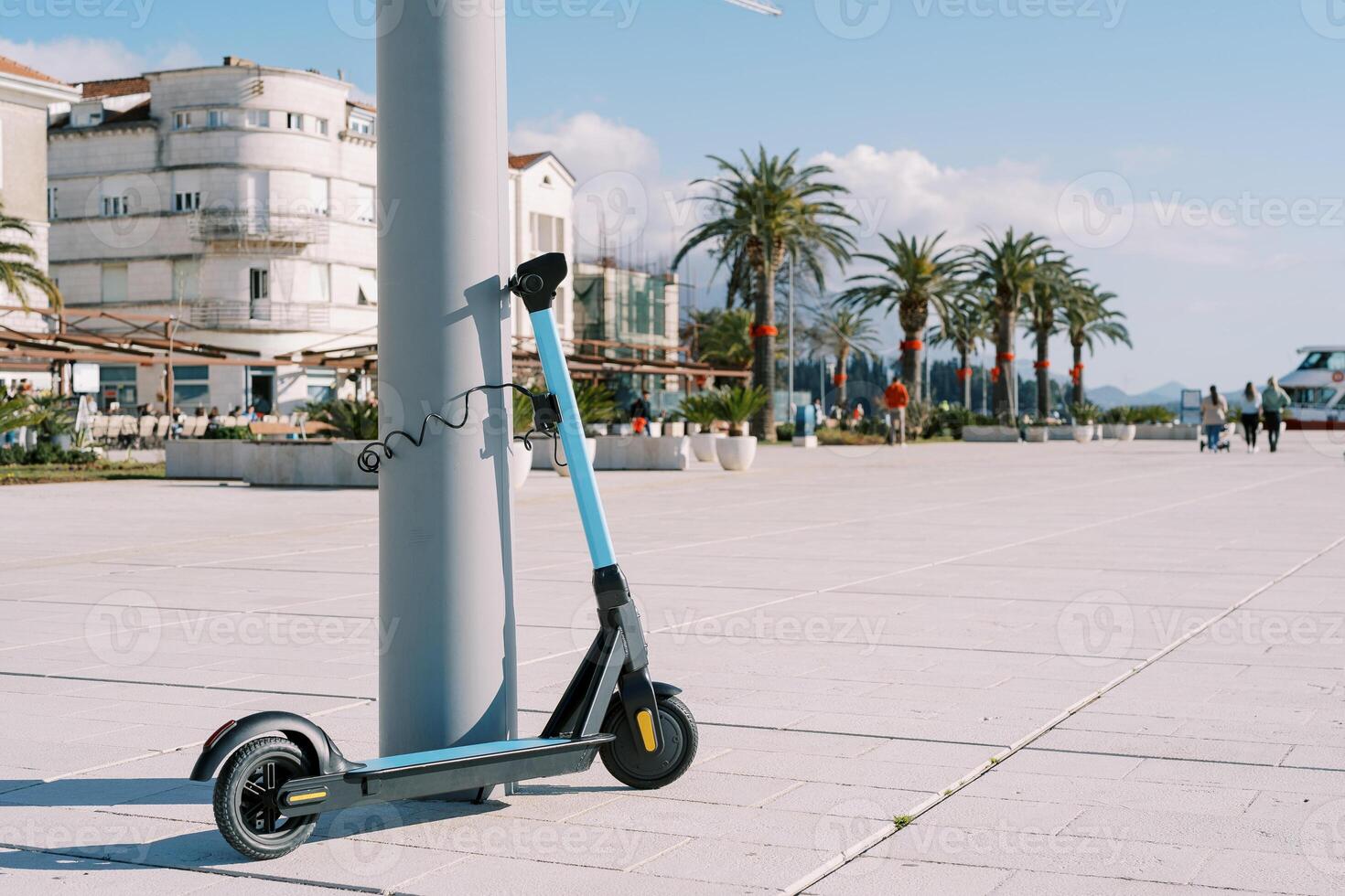 Rental blue electric scooter is fastened to a pole on an embankment with green palm trees photo