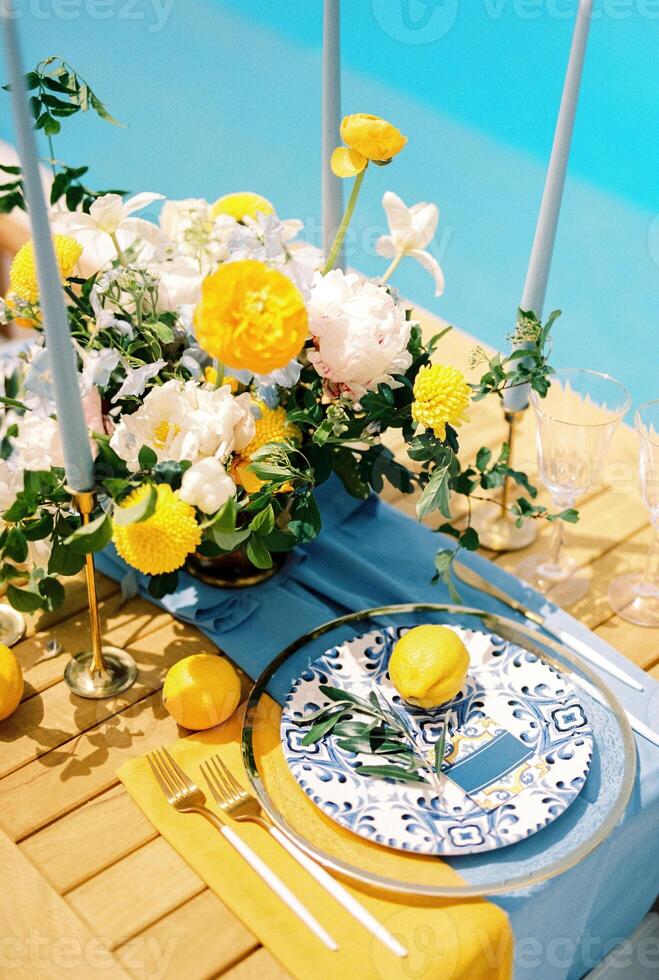 Lemon, olive branch and invitation lie on a plate on a holiday table near a bouquet of flowers photo