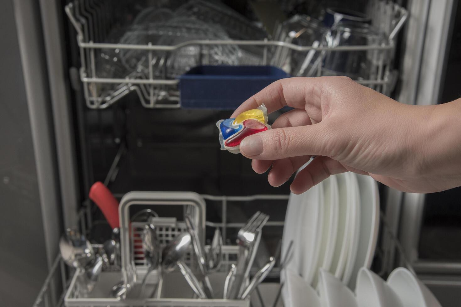 Woman putting detergen kapsul into open dishwasher photo