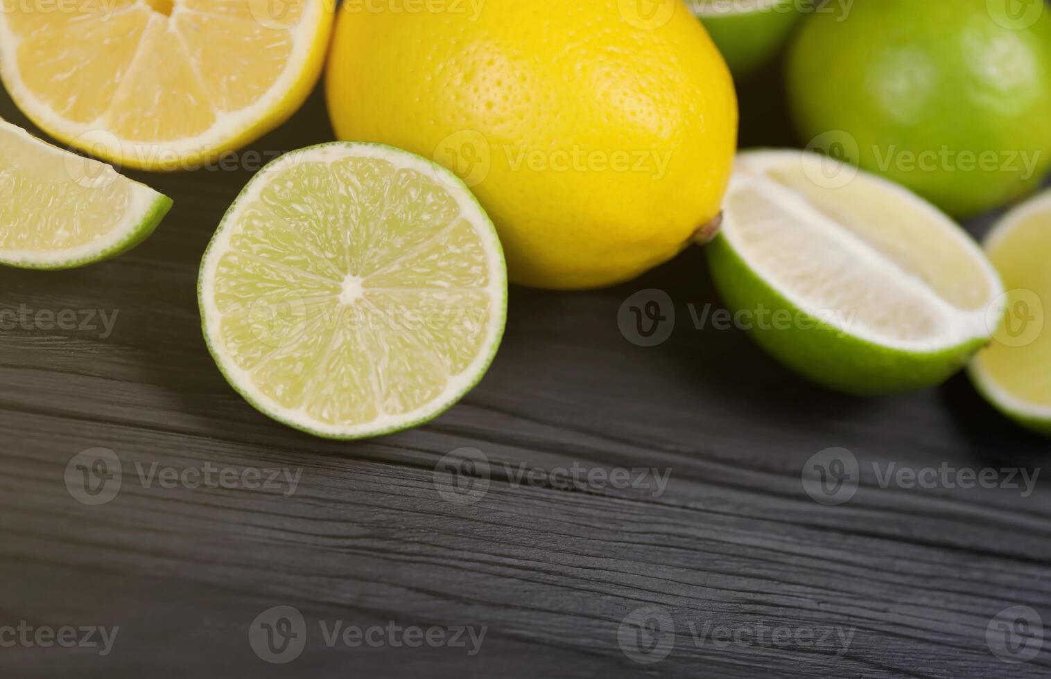 Many halves and slices of yellow lemon and green lime on black wooden table. Fresh fruits on kitchen top with copy space for text photo