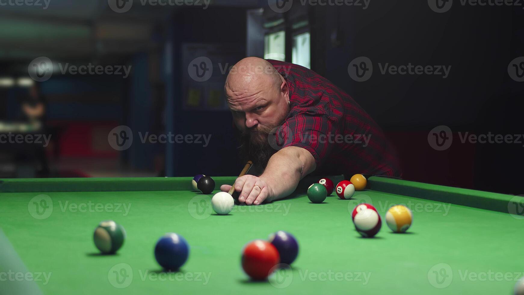 A Big Bald Brutal Bearded Man Plays Billiards On A Green Table, Takes Aim And photo