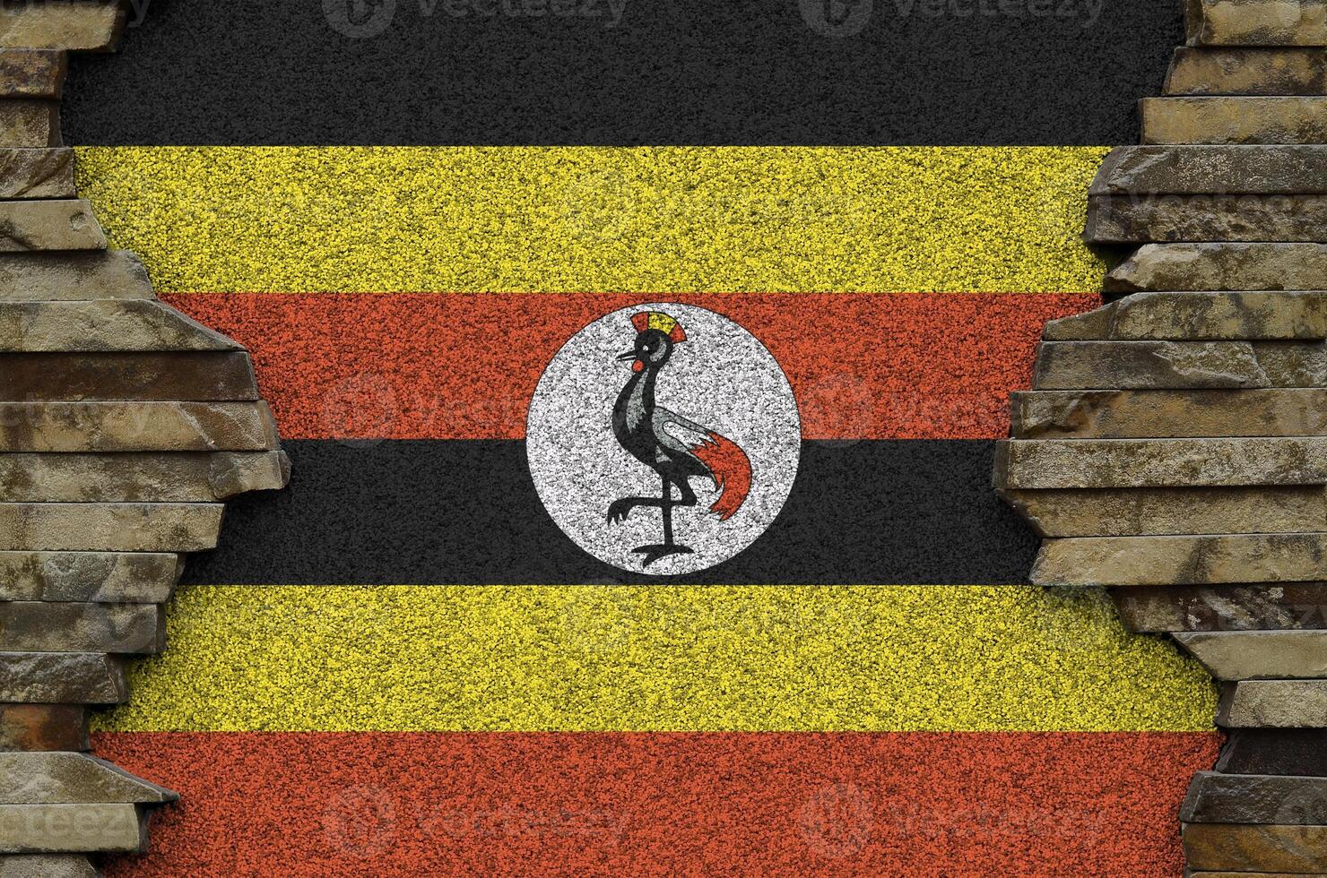 Uganda flag depicted in paint colors on old stone wall closeup. Textured banner on rock wall background photo