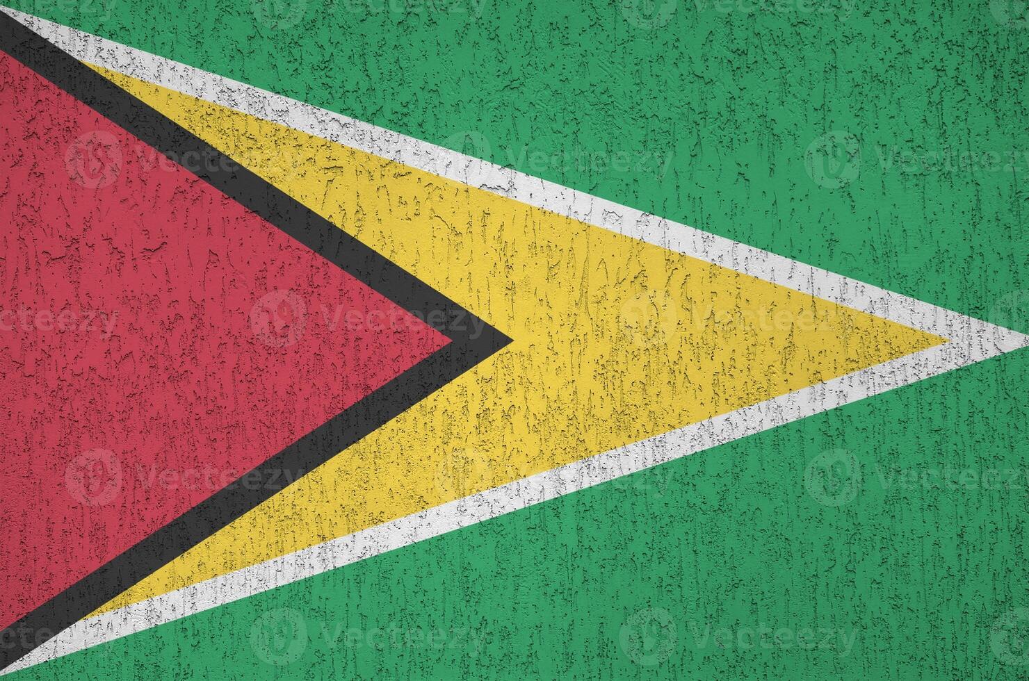 Guyana flag depicted in bright paint colors on old relief plastering wall. Textured banner on rough background photo