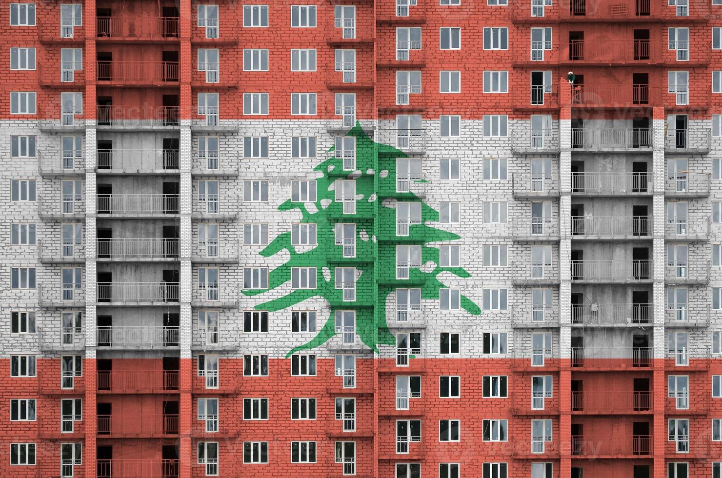 Lebanon flag depicted in paint colors on multi-storey residental building under construction. Textured banner on brick wall background photo