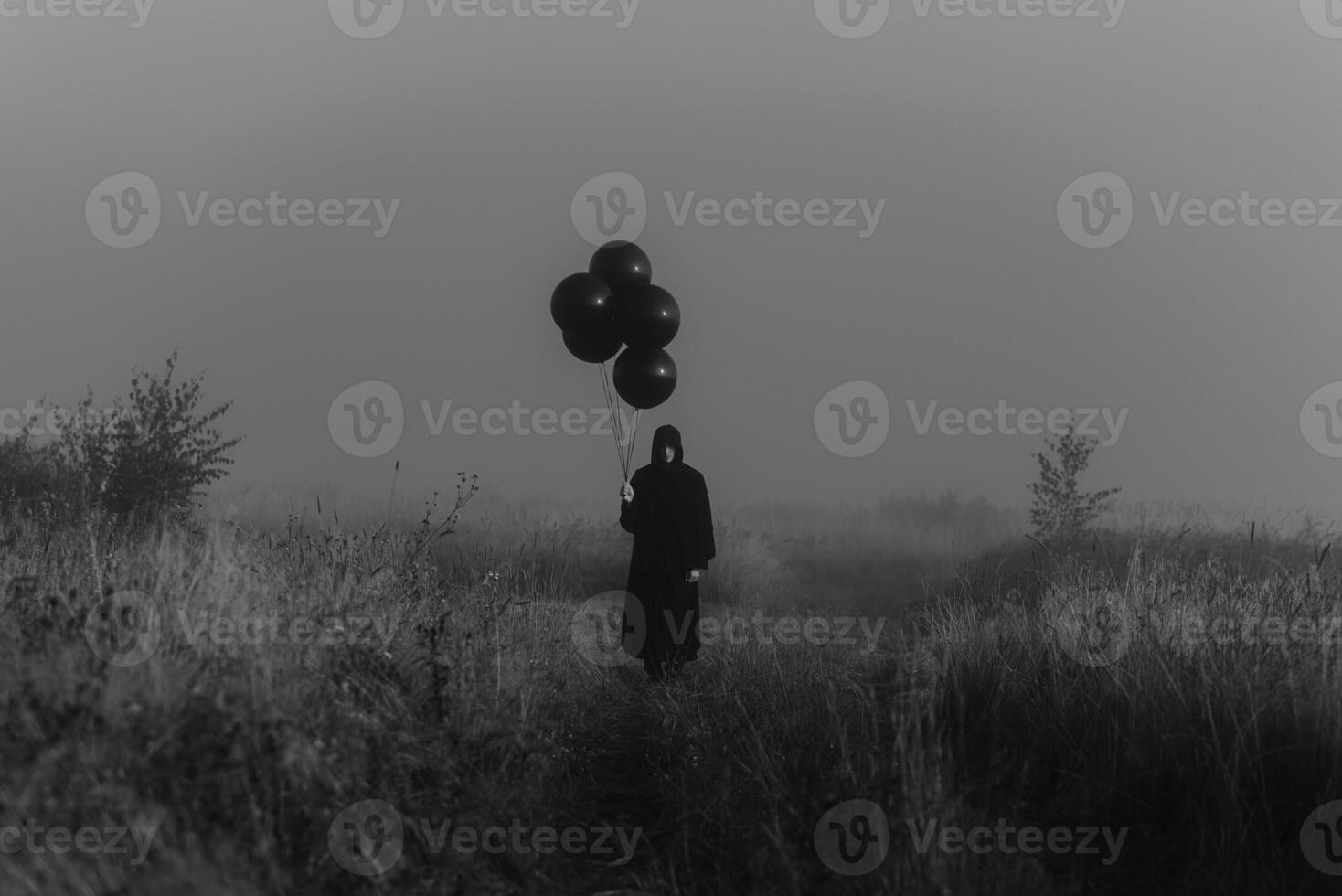 scary dark man in a monster costume with a hood with balloons in his hand photo