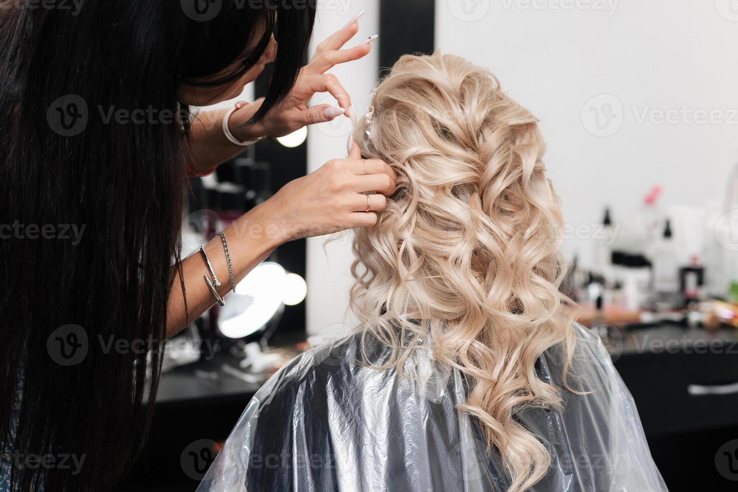 Female hairdresser makes a festive hairstyle for a blonde in a beauty salon. photo