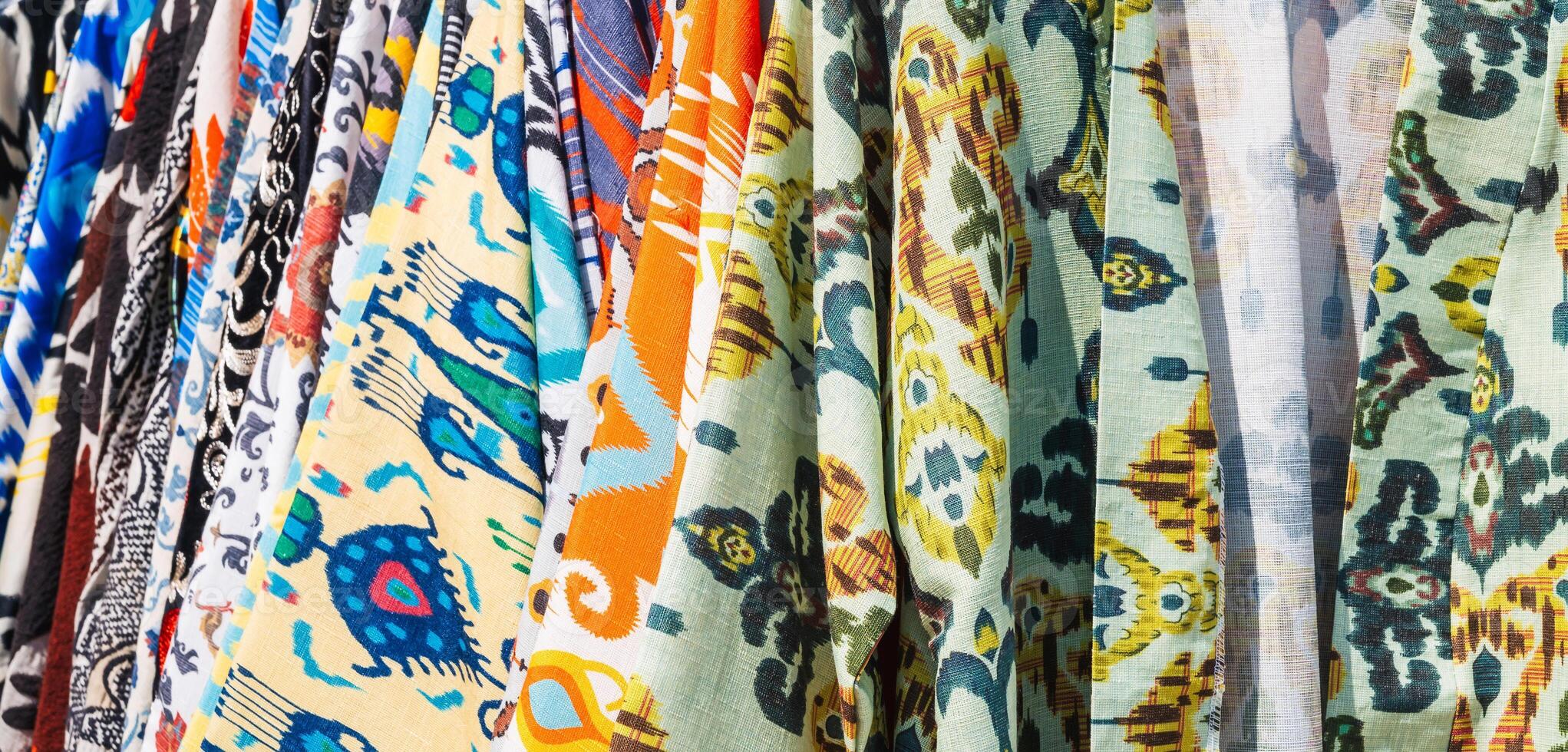 Uzbek dresses and female clothes made of silk and cotton with a colorful pattern at oriental bazaar close up photo