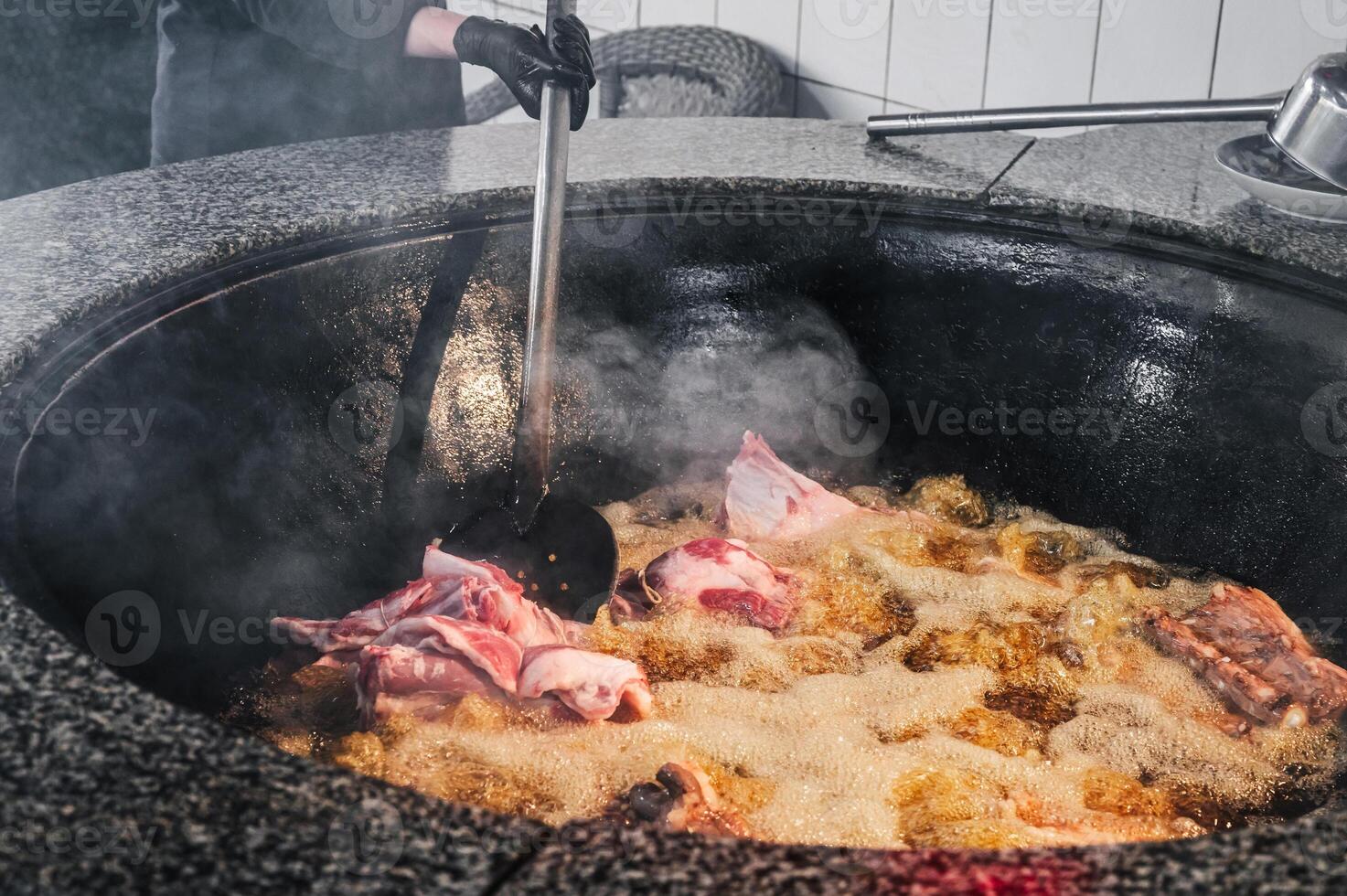 male chef cooks lamb meat in a boiling cauldron for oriental Uzbek pilaf in kitchen in Uzbekistan in Tashkent photo