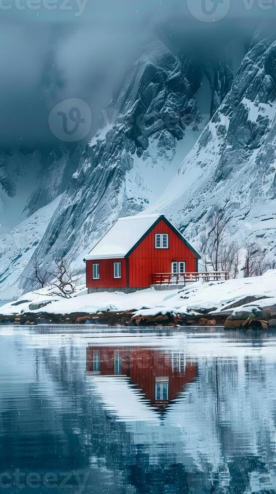 A red house sits on a snowy mountain. The house is surrounded by a beautiful lake and mountains photo