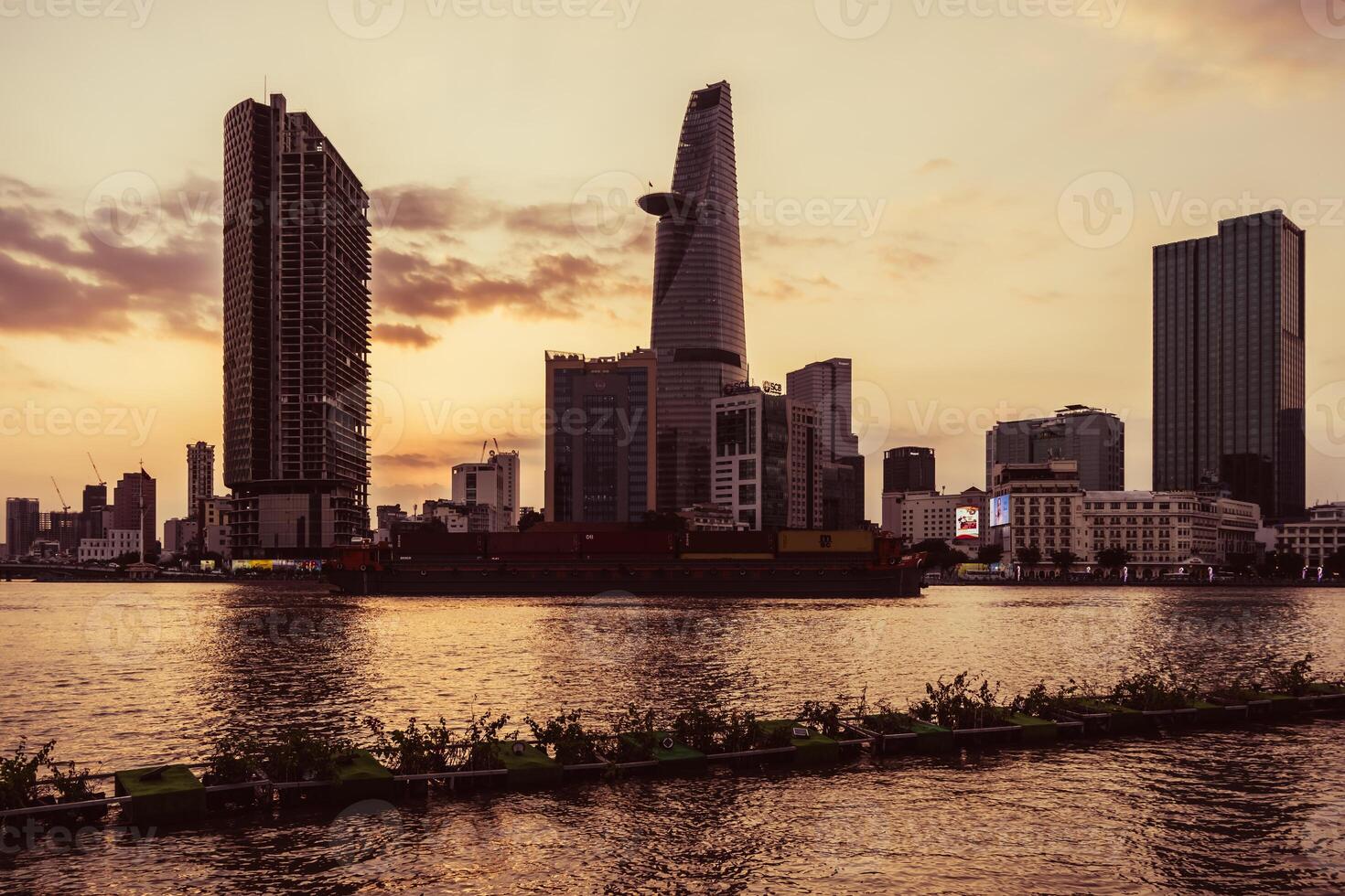 Sunset view of Bitexco Tower, buildings, roads, Bason bridge and Saigon river in Ho Chi Minh city, container cargo ship on Saigon river. Travel concept. photo