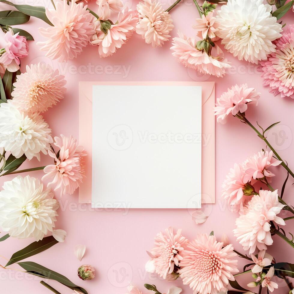Square blank card surrounded by pastel colored flowers on a light pink background in a top view photo