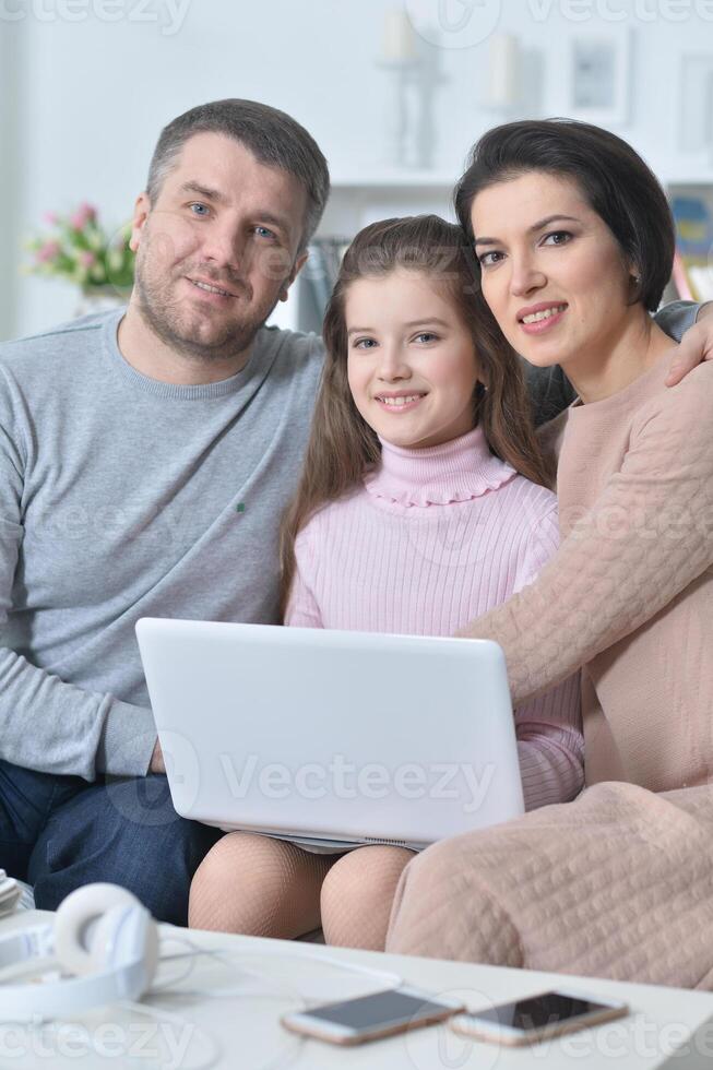 Happy girl sitting at table with laptop with her parents photo