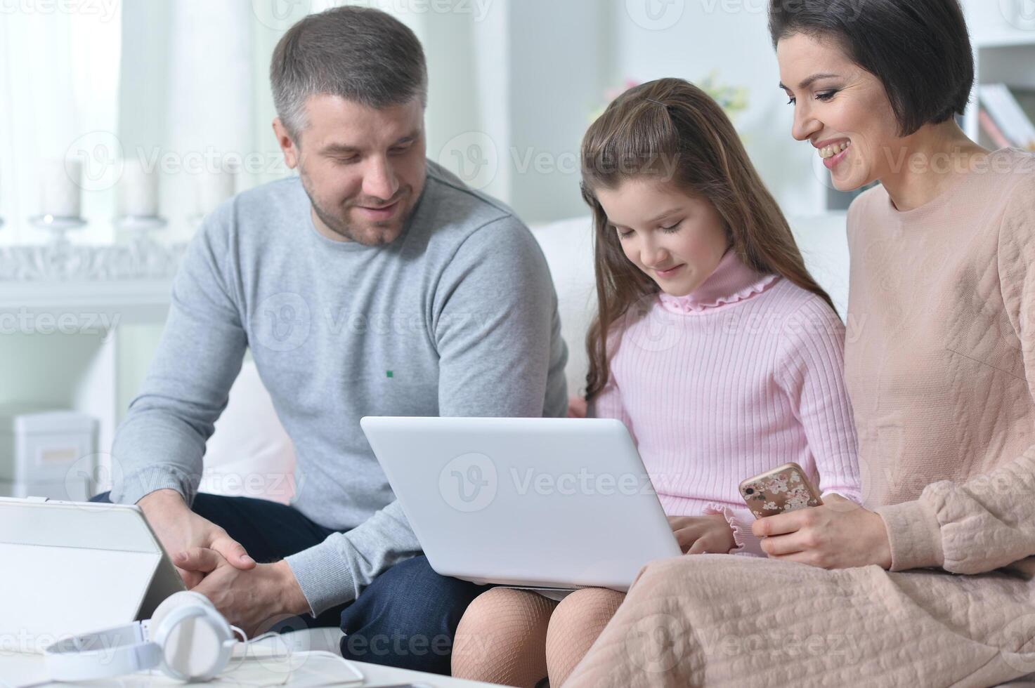 Happy girl sitting at table with laptop with her parents photo