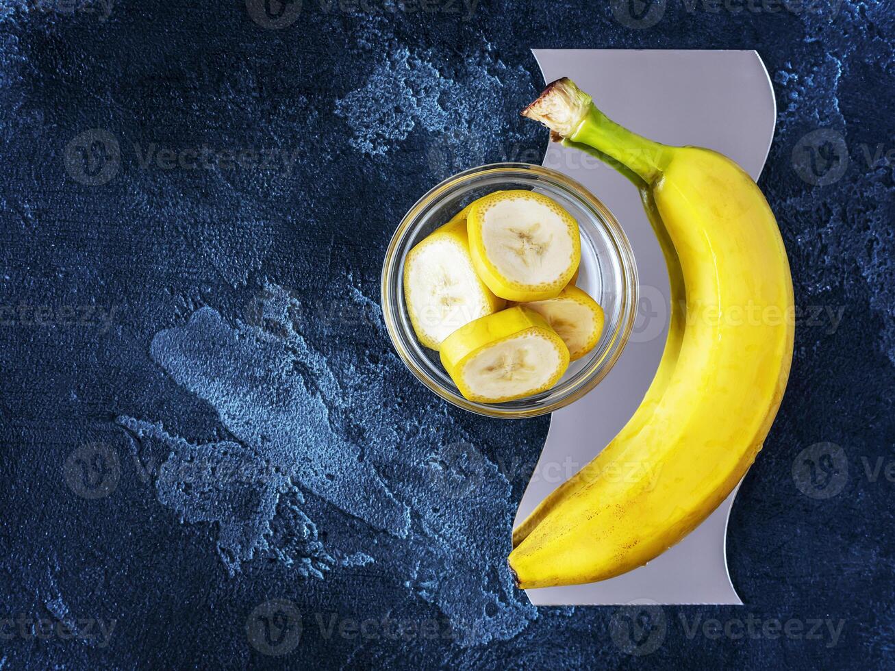 Ripe fresh yellow banana with sliced pieces in a bowl on a textured blue background with copy space photo