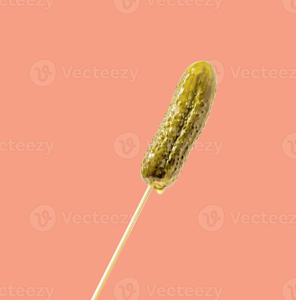 Whole pickle with marinade droplets on a stick on a pink background photo