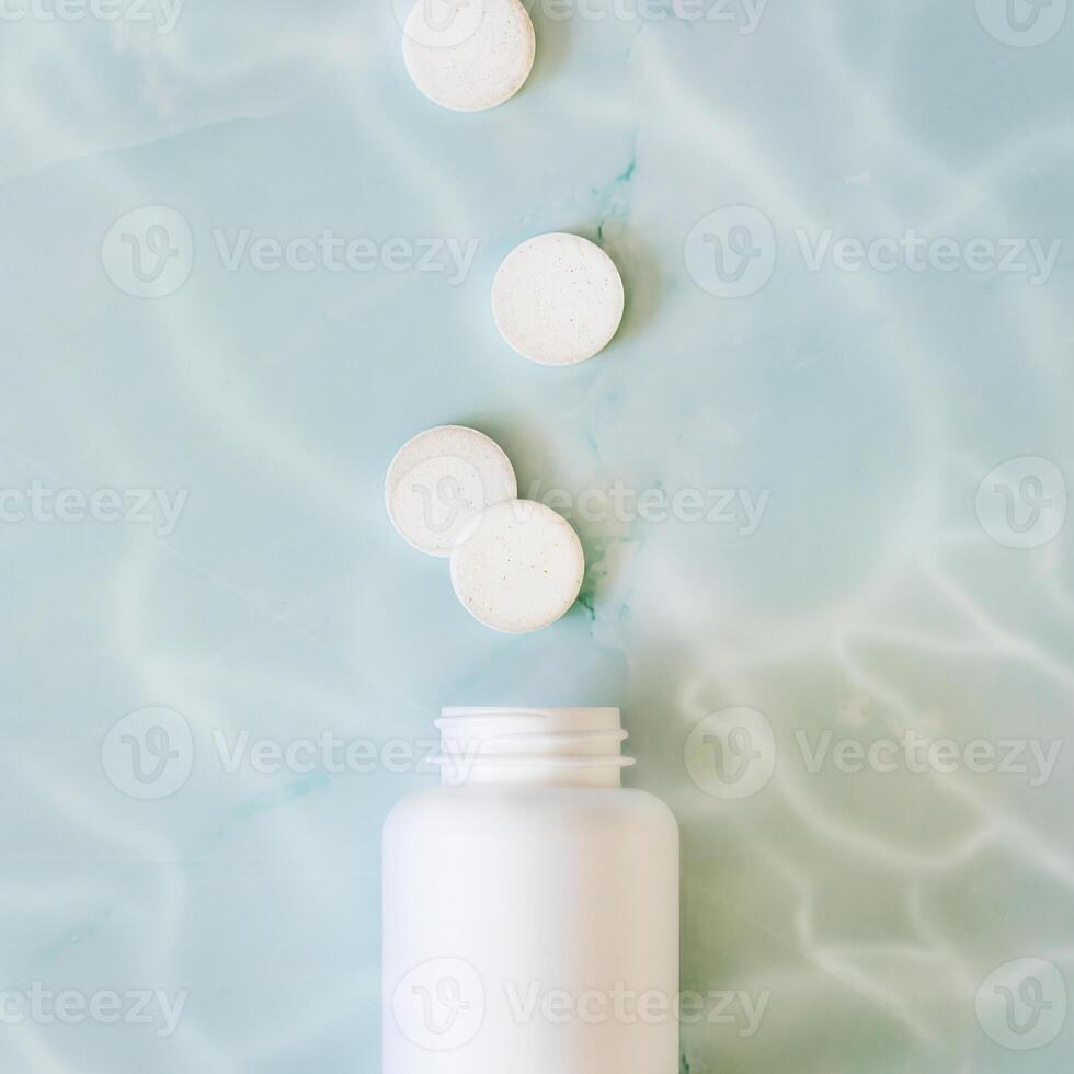 White pills and white bottle with copy space on blue water background photo