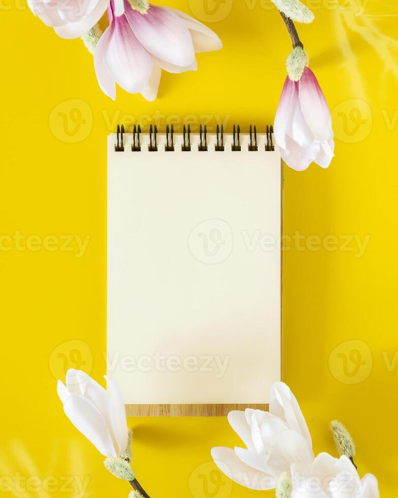 An open notebook with a white blank sheet of paper and branches of a blooming magnolia photo