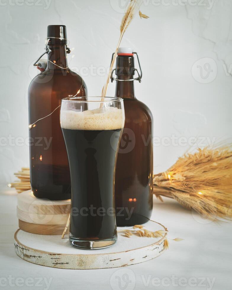 Glass of dark, unfiltered beer, two dark brown bottles and bouquet of wheat on a white background photo