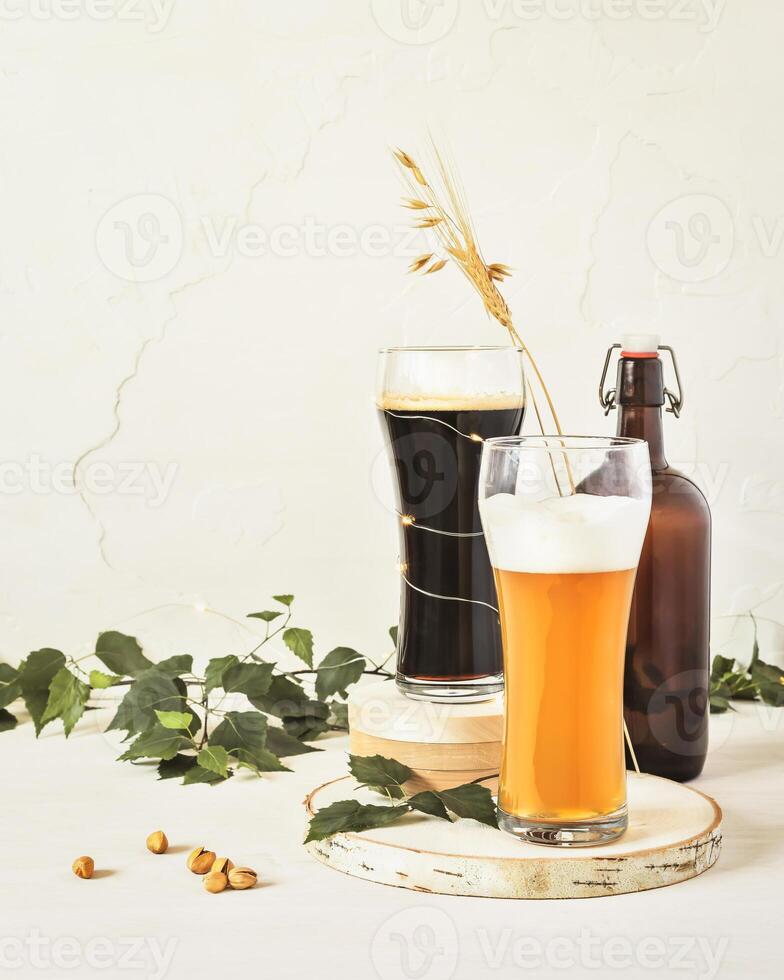 Two glasses of cold, light and dark, unfiltered beer, bottle, pistachios and leaves on a white background photo