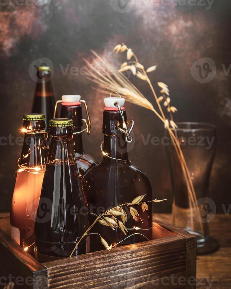 Bottles with cold, light and dark, unfiltered beer with ears of wheat in the empty glass on a broun background photo
